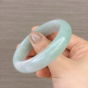 May include: A light green jade bangle bracelet. The bangle is smooth and polished, with a subtle swirl pattern.