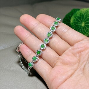 Op de afbeelding: Een zilveren armband met een ketting en groene jade stenen die in zilver zijn gezet. Elke steen is omgeven door kleinere diamanten.