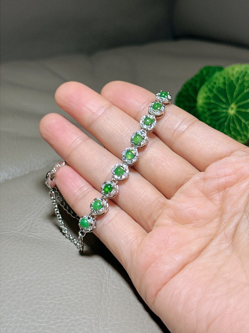 Op de afbeelding: Een zilveren armband met een ketting en groene jade stenen die in zilver zijn gezet. Elke steen is omgeven door kleinere diamanten.