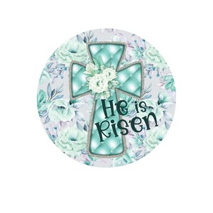May include: A teal blue cross with a quilted design and silver glitter accents is surrounded by white and teal blue flowers. The text "He is Risen" is written in black below the cross.