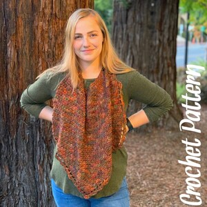 May include: A woman wearing a green shirt and blue jeans is standing in front of a tree. She is wearing a crocheted scarf in shades of orange, brown, and green. The scarf is triangular in shape and has a fringed edge. The text "Crochet Pattern" is written in white on a brown background in the lower right corner of the image.