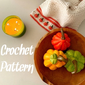 May include: Crochet pattern for a white blanket with a red and orange border featuring a row of crocheted pumpkins. The text "Crochet Pattern" is written in white on a white background. The image also shows a wooden bowl with three decorative pumpkins, a candle, and a sign that reads "Autumn leaves and pumpkins please."