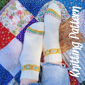 May include: White knitted socks with a crocheted trim in yellow, pink, and blue. The socks are on a patchwork quilt with the words "Knitting Pattern" written on the side.