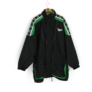 May include: Black and green Reebok jacket with a zipper closure and a drawstring waist. The jacket has a geometric pattern on the shoulders and sleeves.