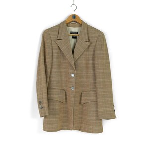 May include: A brown and beige plaid blazer with a single button closure and two pockets. The blazer has a label that reads "ESCADA".