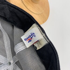 May include: Black mesh baseball cap with a white Reebok logo and a white tag that reads "Unique Product of R.O.C."