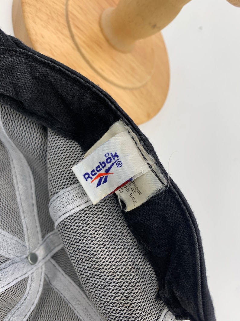 May include: Black mesh baseball cap with a white Reebok logo and a white tag that reads "Unique Product of R.O.C."