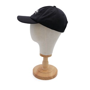 May include: A black baseball cap with a white logo on the front. The cap is on a wooden display stand.