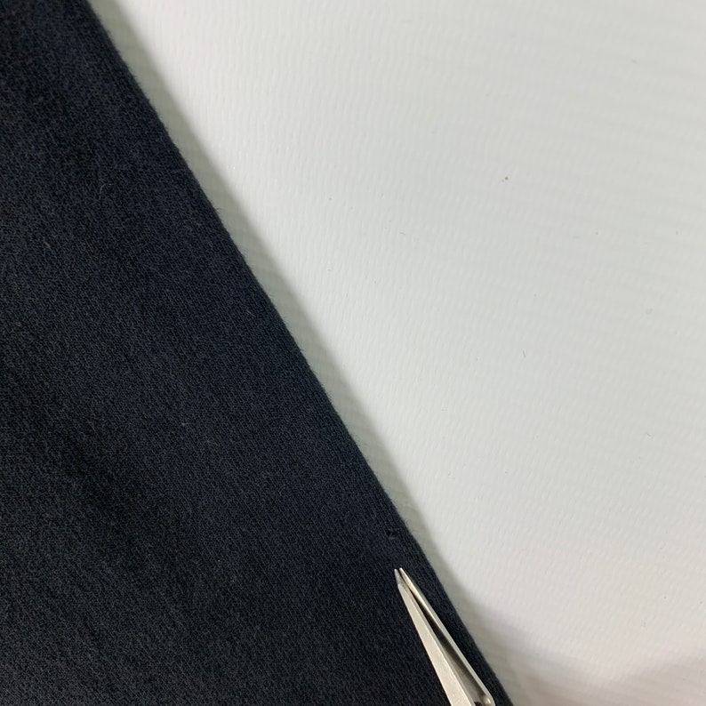 May include: Close-up of black fabric with a small hole in the corner.