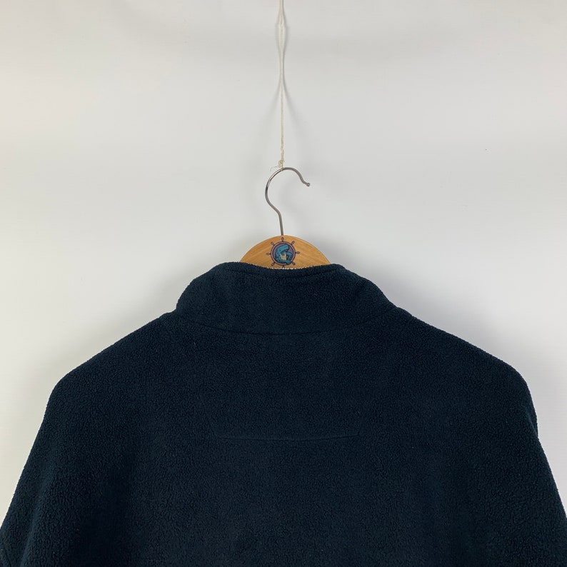 May include: Black fleece jacket with a high collar and a zipper closure. The jacket is hanging on a wooden hanger.