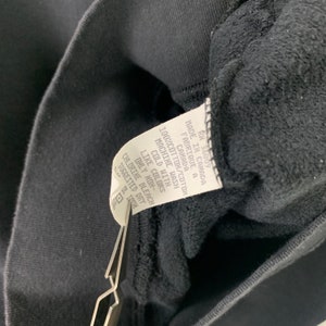 May include: A black care tag with white text that reads: "RN 36009 Made in Canada Fabrique a Canada 100% Cotton/Coton Machine Wash Cold With Like Colors Only Non-Chlorine Bleach Suggested Dry"
