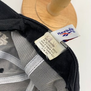May include: Black mesh baseball cap with a white Reebok logo on the front and a white tag on the back that reads "100% Polyester, One Size/Taille Unique, Made in Taiwan R.O.C., Fabrique a Taiwan R.O.C., (3 FW 962)"