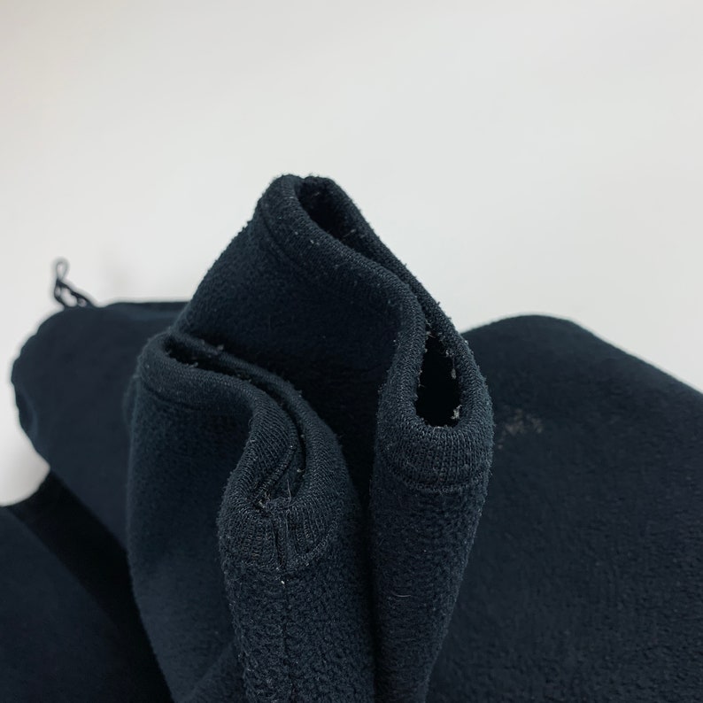 May include: Close-up of black fleece fabric, showing the texture and stitching. The fabric is folded over, revealing the inside of the material.