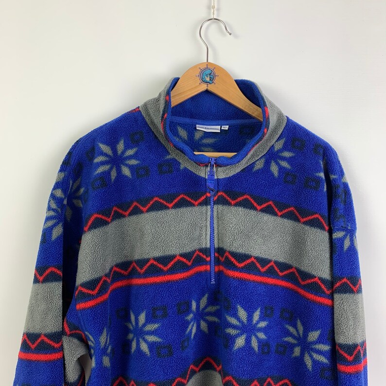 Puede incluir: Un jersey de forro polar azul, gris, rojo y negro con cierre de media cremallera.