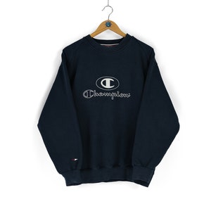Puede incluir: Una sudadera Champion azul marino con un logotipo bordado en blanco que presenta la letra "C" en un círculo y la palabra "Champion" debajo.