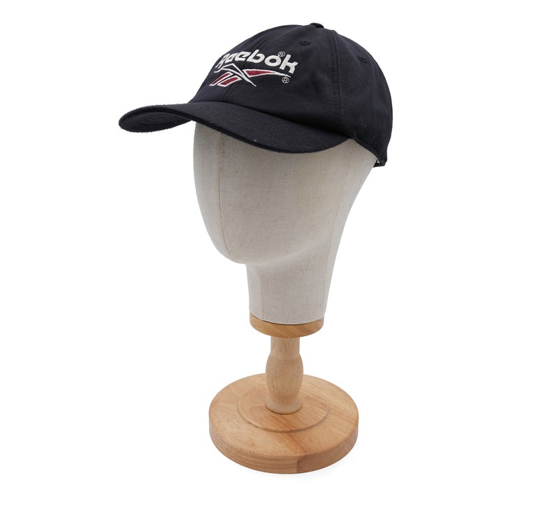 May include: A black baseball cap with a white Reebok logo and a red accent. The cap is on a mannequin head.