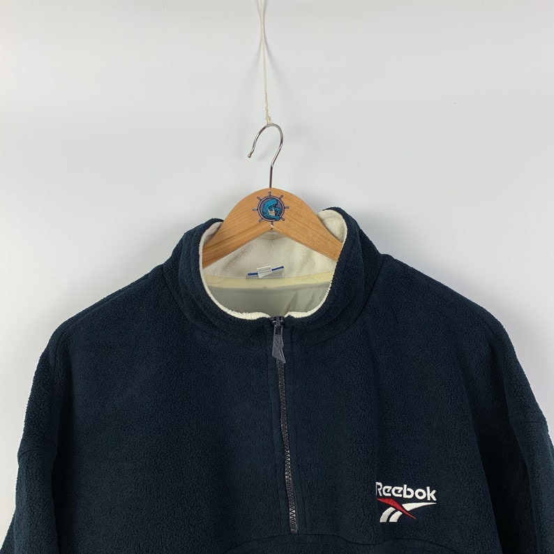 May include: A black fleece pullover with a half-zip closure and a white Reebok logo on the front.