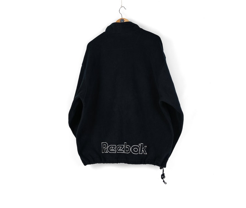 May include: A black fleece jacket with a drawstring at the bottom and a white Reebok logo on the back.