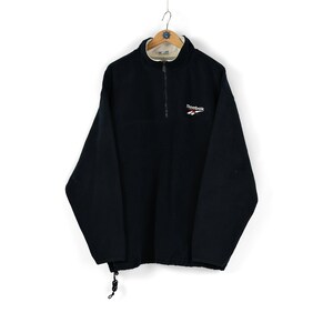May include: A black fleece pullover with a half-zip closure and a small embroidered Reebok logo on the chest.