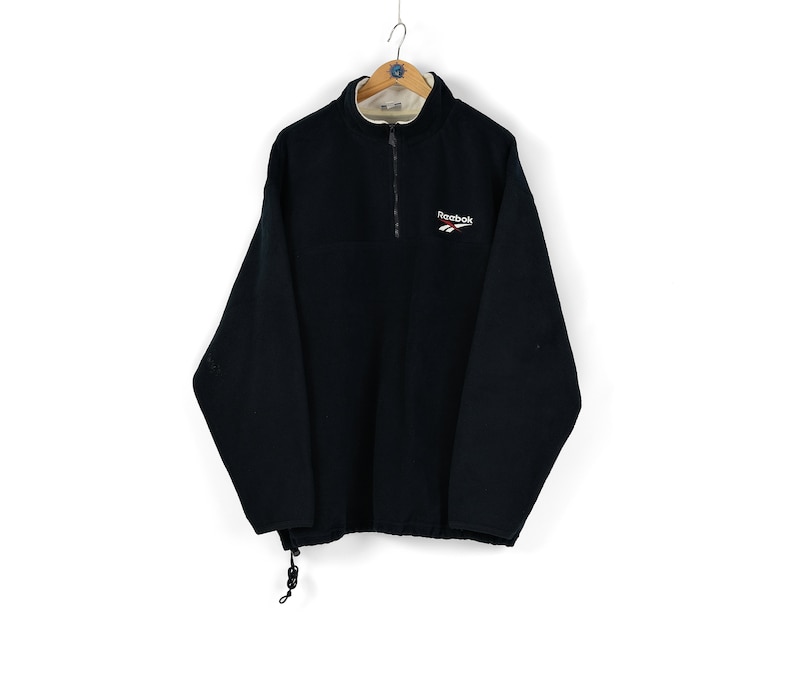 May include: A black fleece pullover with a half-zip closure and a small embroidered Reebok logo on the chest.