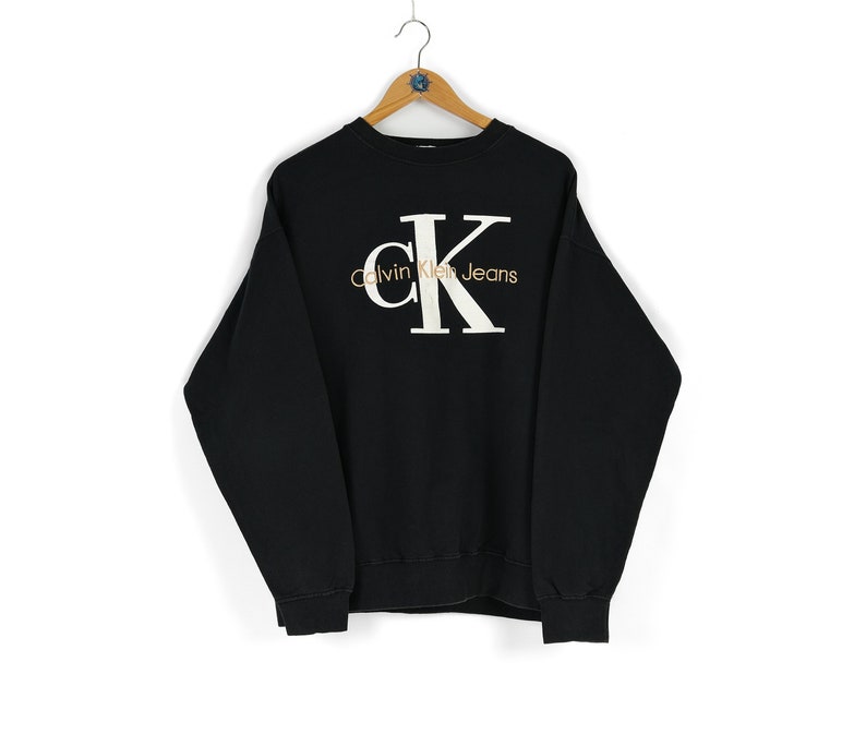 May include: Black sweatshirt with a white Calvin Klein Jeans logo featuring the letters CK in a large, bold font.