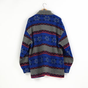 Puede incluir: Una chaqueta de forro polar azul y gris con un patr&oacute;n geom&eacute;trico de copos de nieve. La chaqueta tiene una cremallera y mangas largas.
