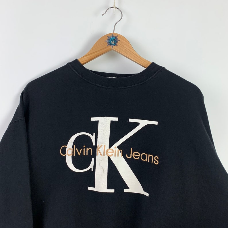 May include: Black sweatshirt with a large white CK logo and the text "Calvin Klein Jeans" in brown lettering.