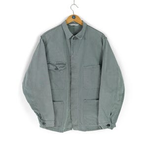 May include: A light green jacket with a button-down front, two chest pockets, and two lower pockets. The jacket is hanging on a wooden hanger against a white background. The sleeves have buttoned cuffs.
