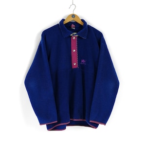 May include: A blue fleece pullover with a snap button placket and a pink and purple Helly Hansen logo.