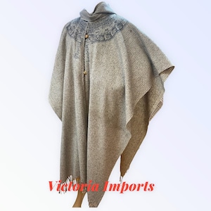 May include: A beige poncho with a textured weave, featuring a hood and decorative embroidery around the neckline. The poncho has a button closure and fringed edges. The text "Victoria Imports" is visible at the bottom.