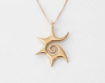 Op de afbeelding: Een goudkleurige hanger met een gestileerde, asymmetrische stervorm en een centraal spiraalontwerp. De hanger hangt aan een fijne, bijpassende goudkleurige ketting en heeft over het hele oppervlak een gladde, gepolijste metalen afwerking.