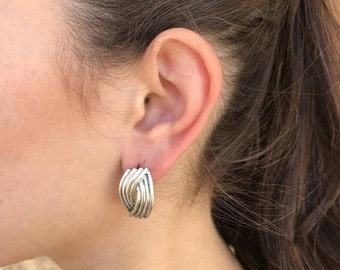 May include: Silver hoop earrings with a woven design. The earrings are a simple and elegant style.