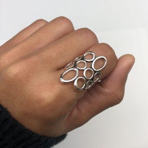 May include: A silver ring with a unique design featuring multiple interconnected circles and ovals. The ring is open and has a delicate, airy look.