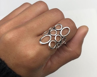 May include: A silver ring with a unique design featuring multiple interconnected circles and ovals. The ring is open and has a delicate, airy look.