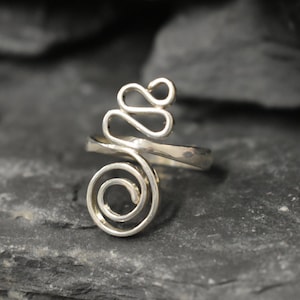 Könnte beinhalten: Ein silberner Ring mit einem einzigartigen, abstrakten Design. Der Ring besteht aus einem einzigen Drahtstück, das zu einer Spirale und einer Reihe von Schleifen gedreht und geformt ist.