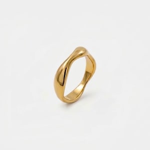 May include: A gold-toned ring featuring a smooth, polished surface with an irregular, organic, wavy silhouette. The band has a continuous, flowing shape that creates a soft, undulating appearance around the entire circumference of the ring.