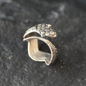 Könnte beinhalten: Silberring mit Schlangenmotiv. Die Schlange ist um den Ring gewickelt und hat eine strukturierte, schuppige Oberfläche.