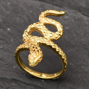 May include: A gold-colored ring with a snake design. The snake is coiled around the ring band and has a detailed, textured surface.