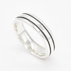 May include: A silver band ring with two black lines around the center of the band.