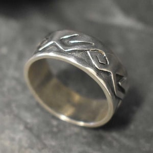 May include: A silver ring with a textured band and a geometric design. The ring is made of sterling silver and has a hammered finish.