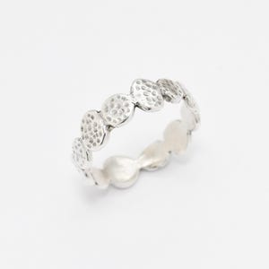 May include: A silver ring with a textured, hammered finish. The ring is made up of a series of small, round, connected pieces.