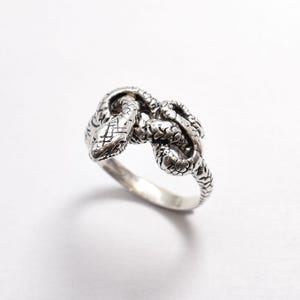 Op de afbeelding: Een zilveren ring met een gedetailleerd slangendesign. De slang is opgerold en zijn kop is naar voren gericht.