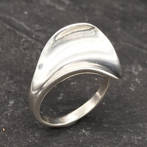 May include: A silver ring with a curved, wave-like design. The ring is smooth and polished.