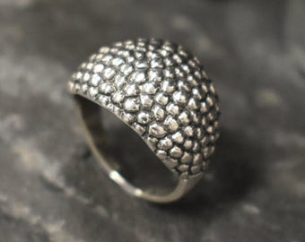 May include: A silver ring with a textured, bumpy surface. The ring is wide and has a rounded top.