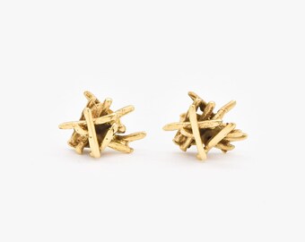 May include: A pair of gold-toned earrings with a unique, abstract design. The earrings are made of thin, interwoven metal pieces that create a textured, organic look.