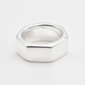 Puede incluir: Un anillo de plata con forma hexagonal. El anillo es liso y pulido.