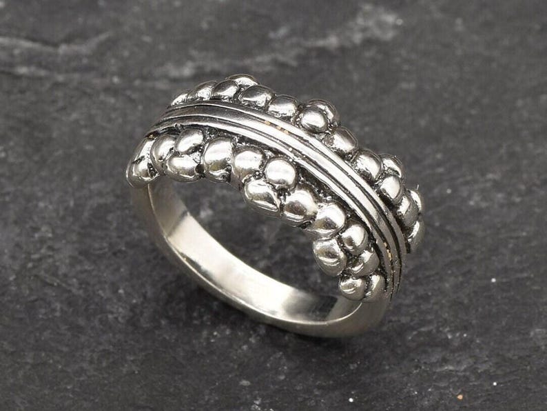 May include: A silver ring with a textured band made of small, round beads. The band is slightly raised and has a subtle groove running along the top.
