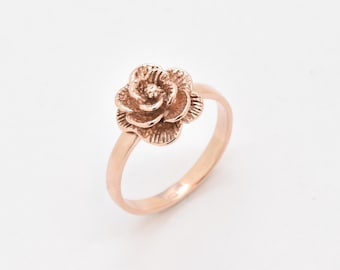 May include: A rose gold ring with a detailed rose design.