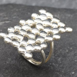 May include: A silver ring with a textured design made of small, round beads. The ring is made of two bands that are connected by the textured design.