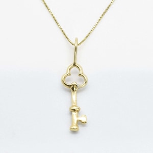 May include: A gold key pendant necklace with a clover-shaped keyhole. The necklace is on a white background.